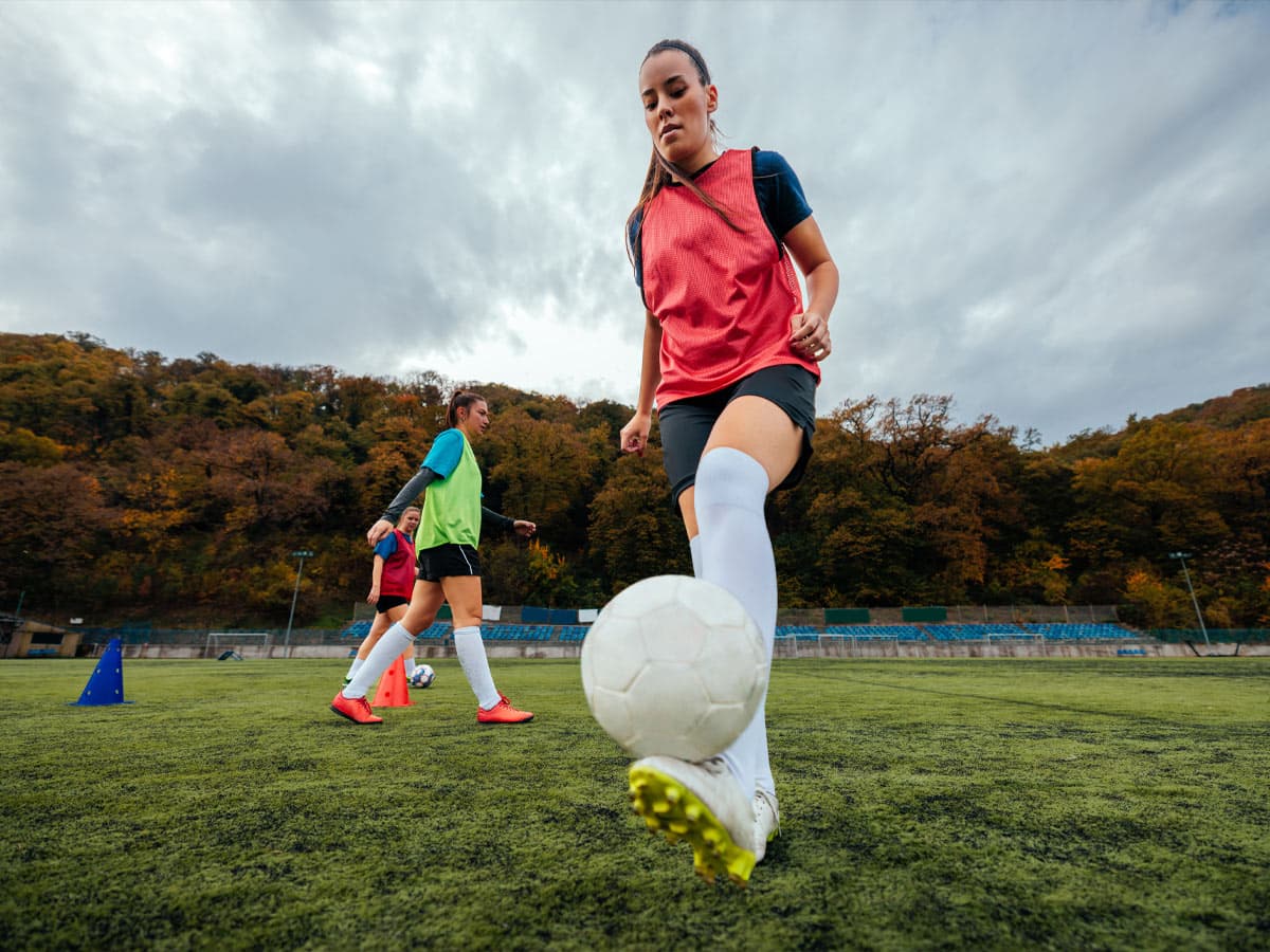 Sieviete sporta tērps uzgrūž futbola bumbu uz zālēra laukuma, parādot savu spēku un koncentrēšanos spēles laikā