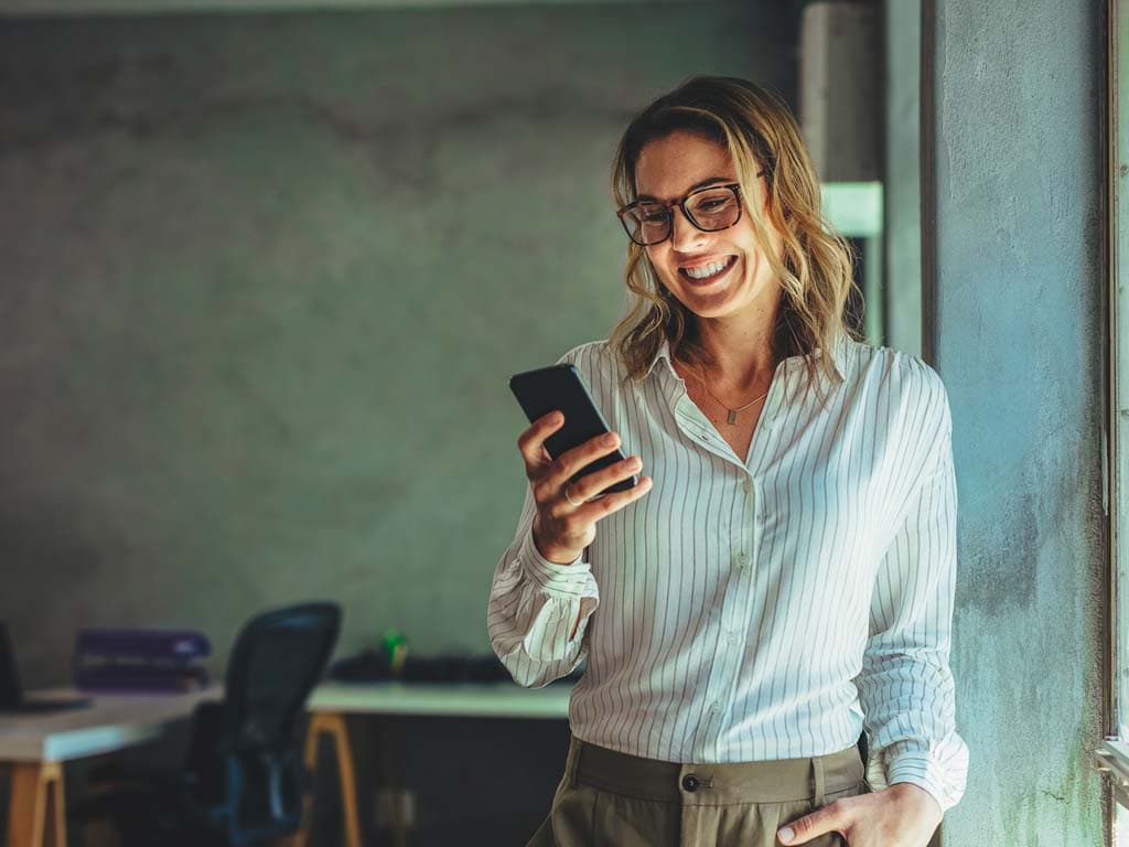 Fokusēta sieviete ar brillēm, tur mobilā tālruņa ierīci
